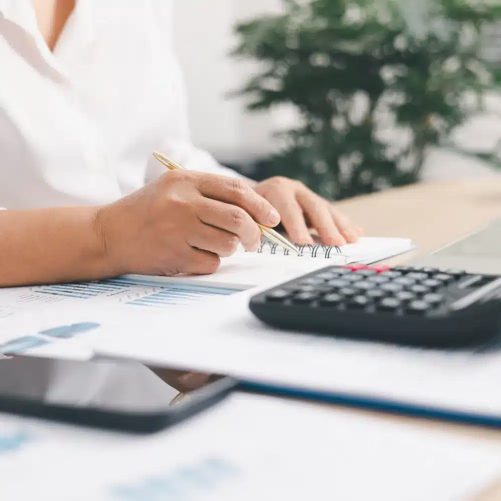 Payroll professional reviewing employee payroll records and accounting documents on a laptop in an office.
